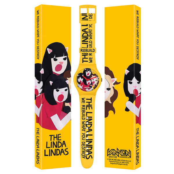 A limited edition yellow wristwatch by The Linda Lindas, featuring Japanese Quartz movement and packaging with cartoon art of four girls. Text reads: THE LINDA LINDAS - WE REBUILD WHAT YOU DESTROY.