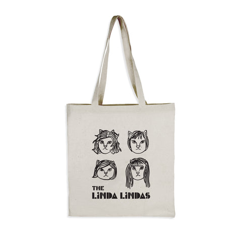 Image of the front of a light tan/off white colored tote bag against a white background. The bag features drawings of 4 different cat faces in black- three have shorter hair and one has longer hair. Below this in black text reads "the linda lindas".