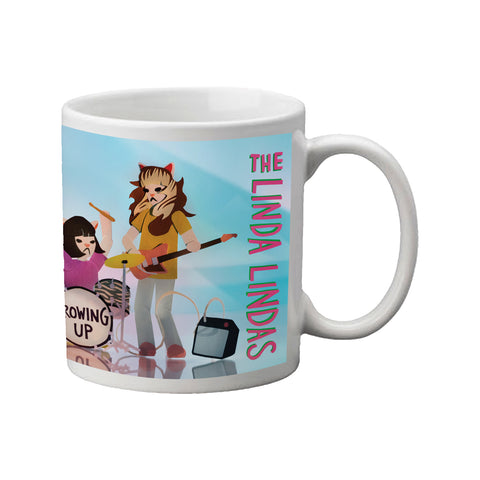Image of a white coffee mug against a white background. The coffee mug features the Linda Lindas- Growing Up album artwork. This photo shows the right side of the artwork- a cartoon character is playing drums, and the other is playing bass. along the side of them in red with green outline it says the linda lindas. the background behind them is light and darker teal.
