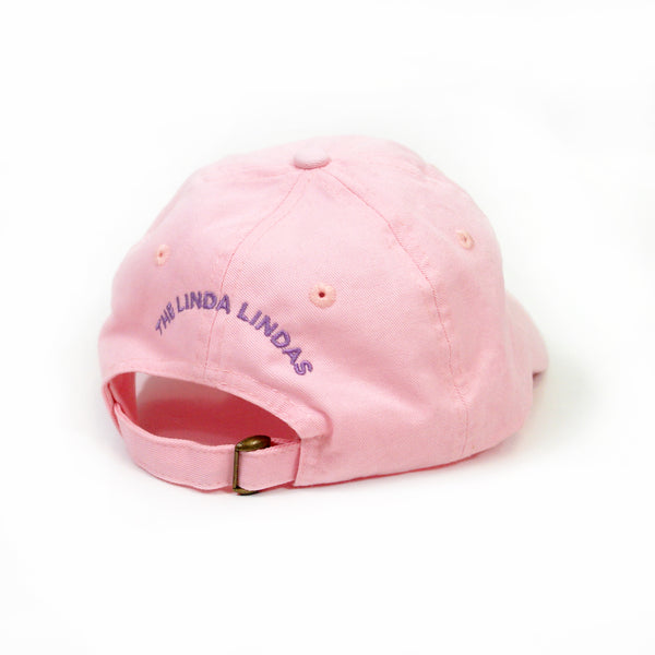 image of the back of a pink dad hat on a white background. back of the hat has purple embroidery that says the linda lindas