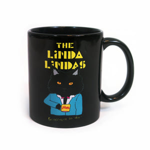 Image of a black coffee mug against a white background.   The Center of the mug says the linda lindas in yellow blocky text. Below that is a graphic of a black cat from the waist up. The cat is wearing a blue suit and holding a cup of coffee. The coffee cup is yellow and says "Nino" in red text. Below this in thin yellow text reads "gentleman by day".