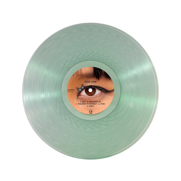  Image of a coke bottle light green colored vinyl against a white background. The center of the vinyl has a sticker of an up close photo of an eye and eyebrow. There is black winged eyeliner on the eyelid to look like a cat. The sticker says Side one, 45 rpm, and lists the first 5 songs on the album.