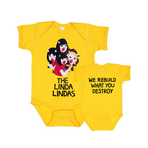 Image of a the front and back of a yellow onesie against a white background. The center of the front of the onesie features a graphic of 4 cats singing. They are drawn from the waist up and all have dark colored hair and red tshirts. Below that in large black text (one word per line) reads "the linda lindas". The back of the onesie in black text reads "we rebuild what you destroy".